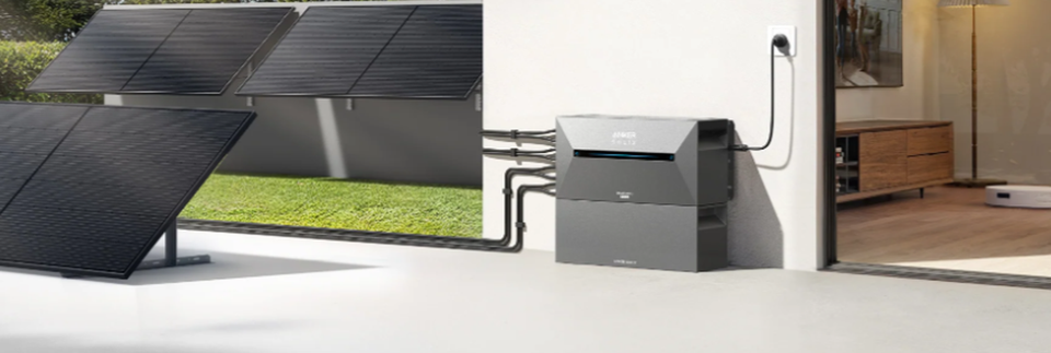 Anker SOLIX Solarbank 2 mit Erweiterungsakku neben Solarmodulen auf einer Terrasse.