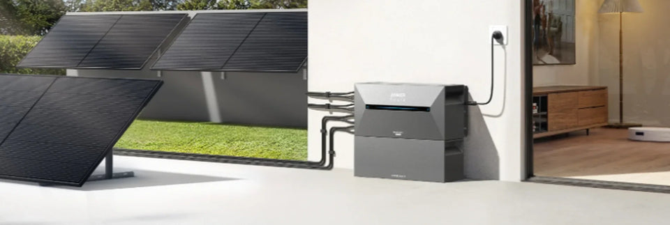 Anker SOLIX Solarbank 2 mit Erweiterungsakku neben Solarmodulen auf einer Terrasse.