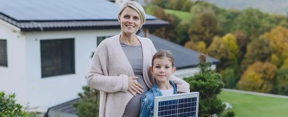 Erwachsene und Kind mit einem kleinen Solarmodul vor einem Haus.